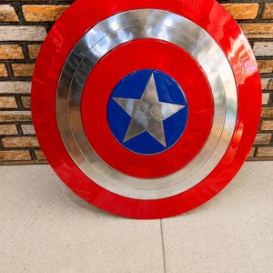 May include: A circular shield featuring a vibrant red outer ring, a metallic silver middle ring, and a deep blue center circle. A prominent five-pointed silver star is centered within the blue circle, creating a bold and symmetrical design.