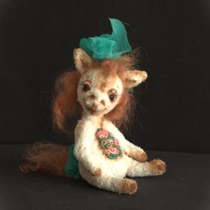 May include: A white stuffed animal with a brown face and long brown hair. The animal is wearing a green bow and has a floral design on its chest.