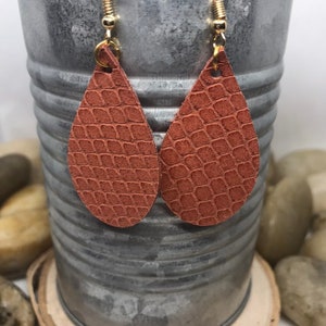May include: A pair of teardrop-shaped earrings made of brown leather with a snakeskin pattern. The earrings have gold hooks.