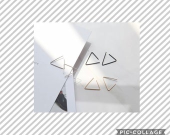 May include: A collection of minimalist triangle-shaped earrings in silver, black, and gold. The earrings are displayed on a white surface with a shadow, showcasing their geometric design. The image is a close-up, highlighting the simple elegance of the jewelry.