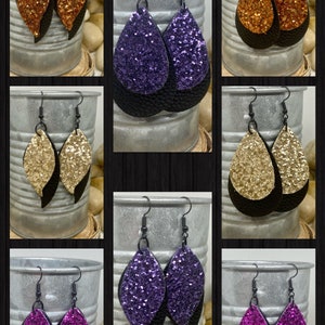 May include: A set of six pairs of dangle earrings. Each pair features two teardrop-shaped pieces of leather. The top piece is covered in glitter and the bottom piece is black leather. The glitter colors are gold, purple, and pink.
