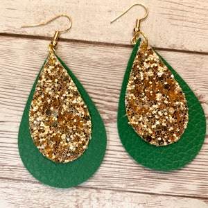 May include: A pair of dangle earrings with a green leather base and gold glitter accents.