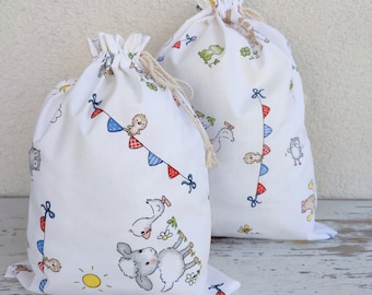 May include: Two white cotton drawstring bags with a farm animal print. The bags feature a variety of animals including a duck, a chick, an owl, and a sheep. The bags have red, blue, and yellow accents.