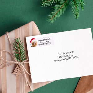 May include: A white envelope with a return address label featuring a golden retriever wearing a Santa hat. The label includes the text "Pregan Benjamin, 1234 Somewhere, Special. Winery 12345". The envelope is addressed to "The Jones Family, 1234 Park Ave., Howardsville, SD 34523".
