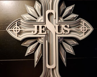 May include: A layered wooden cross with the word "JESUS" in the center. The cross is painted in shades of gray and white.