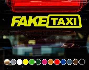 May include: A yellow vinyl sticker with the text "FAKE TAXI" in black lettering. The sticker is on the back window of a car.