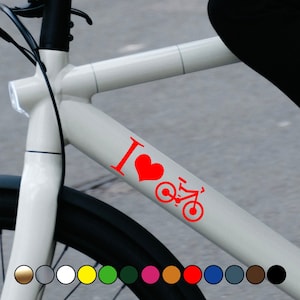 Puede incluir: Un cuadro de bicicleta blanco con una pegatina roja que dice "Me encanta andar en bicicleta". La pegatina presenta un corazón rojo y una silueta de bicicleta roja.