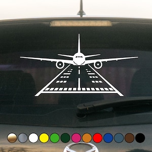 May include: White vinyl decal of an airplane taking off from a runway. The decal is designed to be placed on a car window.