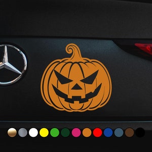 Könnte beinhalten: Orangener Halloween-Kürbisaufkleber mit einem schwarzen Kürbisgesicht. Der Aufkleber befindet sich auf einem schwarzen Auto.