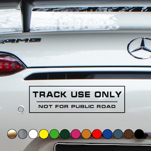 Könnte beinhalten: Das Heck eines weißen Autos mit einem rechteckigen Aufkleber. Der schwarz-weiße Aufkleber lautet "TRACK USE ONLY" und "NOT FOR PUBLIC ROAD". Ein Mercedes-Benz-Emblem ist sichtbar.