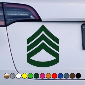 May include: A green military rank insignia sticker with three chevrons. The sticker is on a white car.