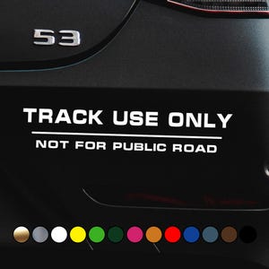 Könnte beinhalten: Schwarzer Autoaufkleber mit weißem Text "TRACK USE ONLY" und "NOT FOR PUBLIC ROAD". Ein silbernes "53"-Emblem befindet sich über dem Text. Am unteren Rand befindet sich eine Reihe von Farbmustern.