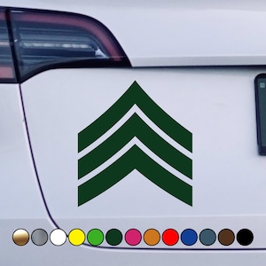 Puede incluir: Pegatina verde de insignia de rango militar con tres rayas. La pegatina está en un coche blanco.