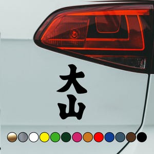 Puede incluir: Calcomanía de vinilo negro con los caracteres japoneses para "大山" (Ooyama) en un coche blanco. La calcomanía se coloca en la parte trasera del coche, cerca del faro trasero. La calcomanía está disponible en una variedad de colores.