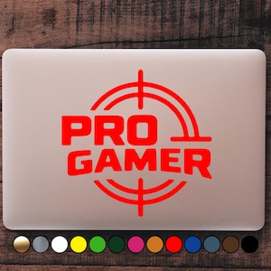 Könnte beinhalten: Ein roter "PRO GAMER" Aufkleber auf einem Laptop. Der Text befindet sich in einem Fadenkreuz-Design. Der Laptop ist hellgrau, mit einer Reihe von Farbmustern am unteren Rand.