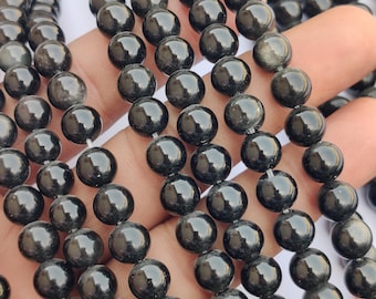 May include: Strands of polished, round, black gemstone beads. The beads have a glossy, reflective surface, and are strung together on a white string. The beads are a dark, solid color, with a subtle sheen.