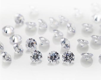 May include: A collection of clear round gemstones, scattered on a white surface. The gemstones are various sizes and have a brilliant shine.