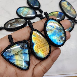 May include: A collection of labradorite gemstone pendants in a variety of shapes and sizes. The pendants are strung on black cords and have an iridescent blue, green, and gold colour.
