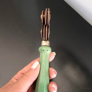 May include: A vintage green handled tool with three metal wheels. The tool is used for cutting fabric.