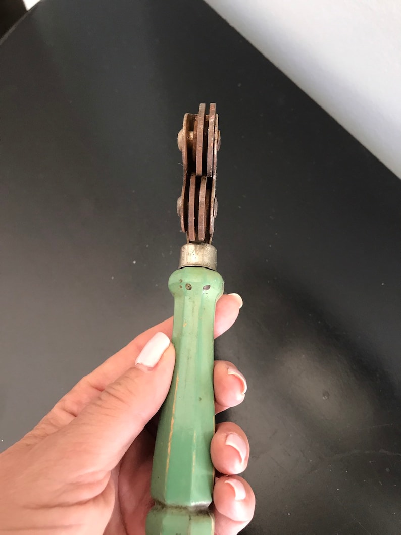May include: A vintage green handled tool with three metal wheels. The tool is used for cutting fabric.