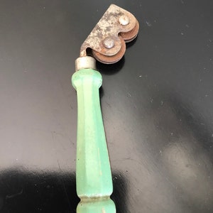 May include: A vintage green handled knife sharpener with two metal wheels. The wheels are rusty and have a heart shape.