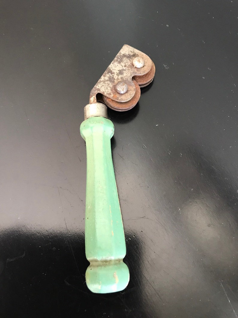 May include: A vintage green handled knife sharpener with two metal wheels. The wheels are rusty and have a heart shape.