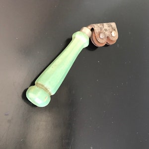 May include: A vintage green handled knife sharpener with two metal wheels. The wheels are rusty and have a worn look.