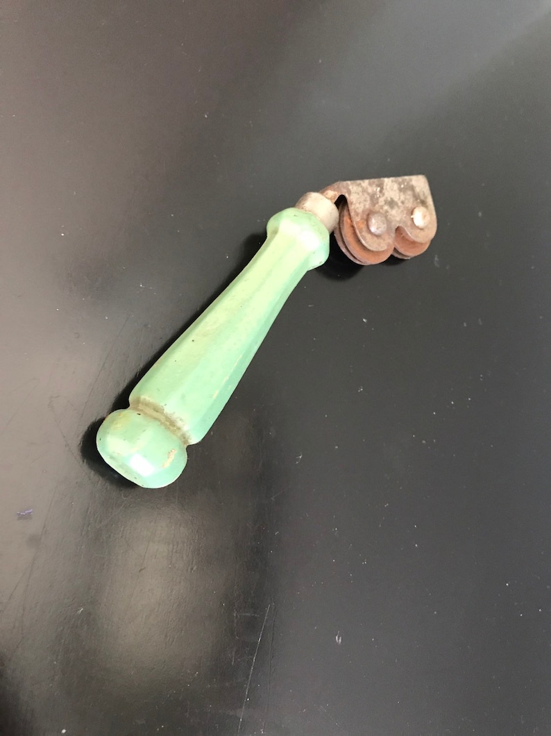 May include: A vintage green handled knife sharpener with two metal wheels. The wheels are rusty and have a worn look.