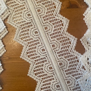 May include: White lace trim with a scalloped edge. The lace has a delicate pattern of small squares and circles.