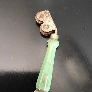 May include: A vintage green handled roller for sharpening knives. The roller has two metal wheels with a metal frame.