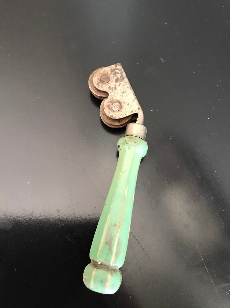 May include: A vintage green handled roller for sharpening knives. The roller has two metal wheels with a metal frame.