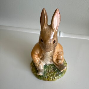 May include: A brown and white ceramic figurine of a rabbit sitting on a green base. The rabbit has brown fur, pink ears, and black eyes.