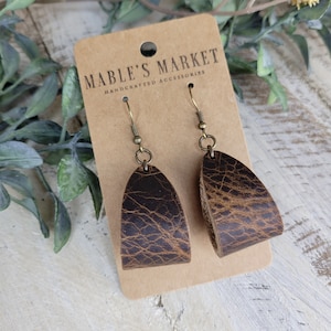 May include: A pair of brown leather earrings with a distressed finish. The earrings are hanging from a card that says "Mable's Market Handcrafted Accessories".