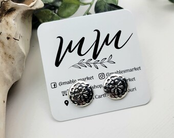 May include: A pair of silver earrings with a floral design. The earrings are on a white card with the text "mmm" and social media handles for @mablemarket.
