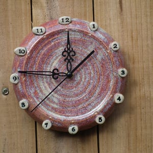 May include: A red and white ceramic clock with black hands and black numbers. The clock is mounted on a wooden wall.