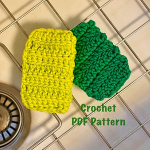 Pode incluir: Dois panos de cozinha de crochê, um amarelo e outro verde, são exibidos em uma grade de metal. O texto "Crochet PDF Pattern" está escrito abaixo dos panos.