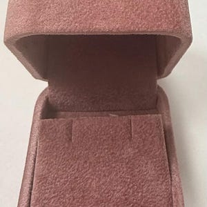May include: A dusty rose velvet ring box with a hinged lid and a soft, plush interior.