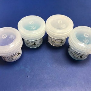 May include: Four small clear plastic jars with white lids containing blue liquid. The jars are labeled "Pen Pals" with different karat gold plating solutions: 14K, Rose, 24K.