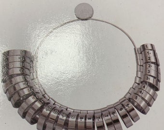 May include: A silver ring sizer with 15 rings, numbered 1 to 15, for measuring ring sizes. The rings are connected by a silver chain.