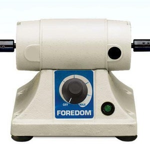 May include: A white Foredom bench grinder with a black knob and a green light. The grinder has two black spindles with a tapered end.