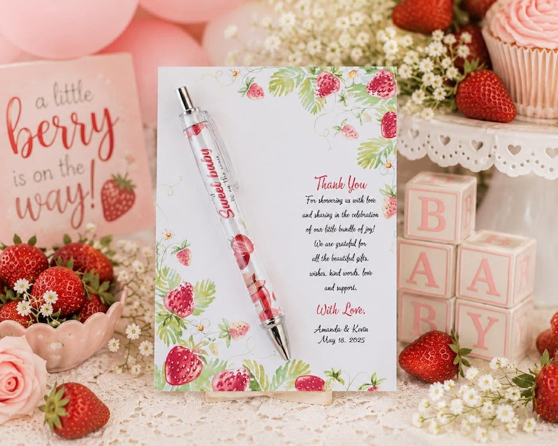 May include: A white thank you card with a strawberry and green leaf border, featuring the text Thank You, For showering us with love, With Love, Amanda & Kevin, May 18, 2025, paired with a clear pen containing floating red strawberry charms.