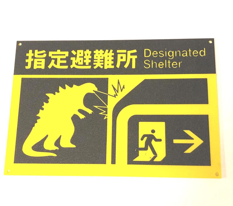 Puede incluir: Un letrero amarillo y negro con las palabras "Designated Shelter" y caracteres japoneses. El letrero presenta una silueta amarilla de un monstruo que respira fuego, una persona corriendo hacia una salida y una flecha.