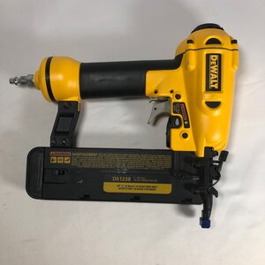 Op de afbeelding: Een gele en zwarte DeWalt D51238 18-Gauge Brad Nailer. De spijkerpistool is ontworpen om alleen 18-gauge bevestigingsmiddelen te accepteren. De spijkerpistool heeft een veiligheidswaarschuwingsetiket en een trekker.