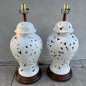May include: A pair of white ceramic table lamps with intricate leaf designs. The lamps have a brown wooden base and a white shade.