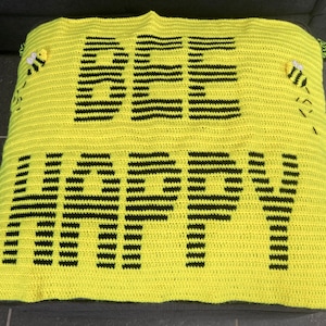 May include: A yellow crocheted blanket with black stripes spelling out "BEE HAPPY" with two small crocheted bees on the top corners.