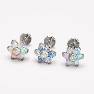 May include: Three silver-toned flat back stud earrings shaped like flowers. Two earrings feature six iridescent white opal-like stones surrounding a central stone. The middle earring features alternating blue and clear stones around a central opal-like stone.