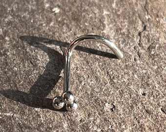 May include: A silver nose ring with three small balls at the end.