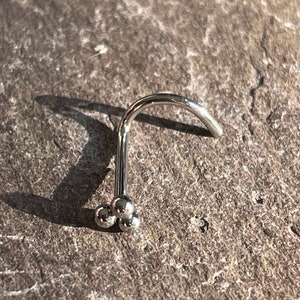 May include: A silver nose ring with three small balls at the end.