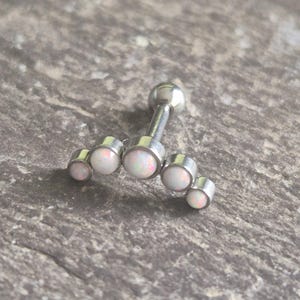 May include: A silver-toned metal body jewellery piece featuring a curved bar design adorned with five round, white opalescent stones of varying sizes arranged in an arch, attached to a straight post with a small spherical end ball.