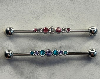 May include: Two silver barbell piercings with colorful gemstones. The top barbell has pink and clear gemstones, while the bottom barbell has blue and purple gemstones.